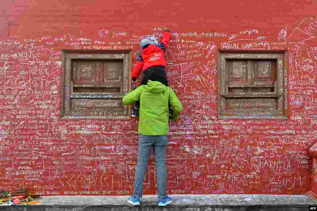 A child, helped by his father, writes a message with chalk on a wall at the Saraswati temple on the occasion of the Hindu festival of 'Basanta Panchami', in Kathmandu, Nepal.