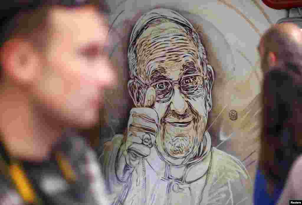 Orang-orang melewati sebuah mural karya seniman jalanan Perancis, Christian Guemy, juga dikenal sebagai C215, yang menggambarkan Paus Francis mengacungan jempol, di sebuah stasiun kereta bawah tanah di Roma. Mural ini terletak dekat loket tiket di stasiun kereta bawah tanah di Spanish Steps, salah satu tujuan wisata terpopoler di ibukota Italia itu. 