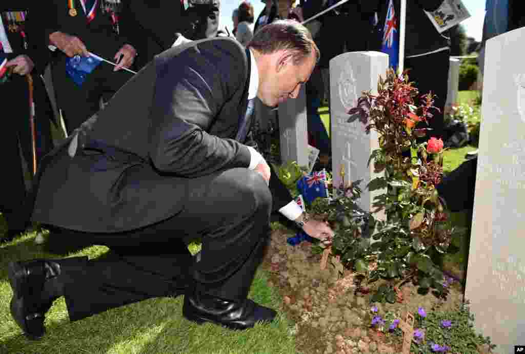 Australia's Prime Minister Tony Abbott places a cross at a grave as he arrives to attend the French-British ceremony at the British War cemetery in Bayeux, Normandy, France, June 6, 2014.