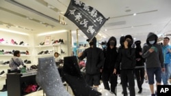 香港黑衣抗议者在铜锣湾的一个商场里举“光复香港，时代革命”的旗子示威。（2019年12月26日）