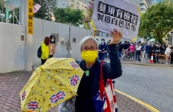 64歲的示威者黃婆婆手持標語及黃傘12月2日到西九龍裁判法院外聲援被判入獄的黃之鋒、林朗彥及周庭.