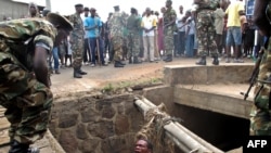 FILE - A man begs for help from the military as he stands in a drain where he had hidden to escape a lynch mob at the Cibitoke district of Burundi's capital, Bujumbura. International judges have approved the opening of a full investigation into alleged crimes against humanity in Burundi, where at least 1,200 people have died in unrest since 2015.