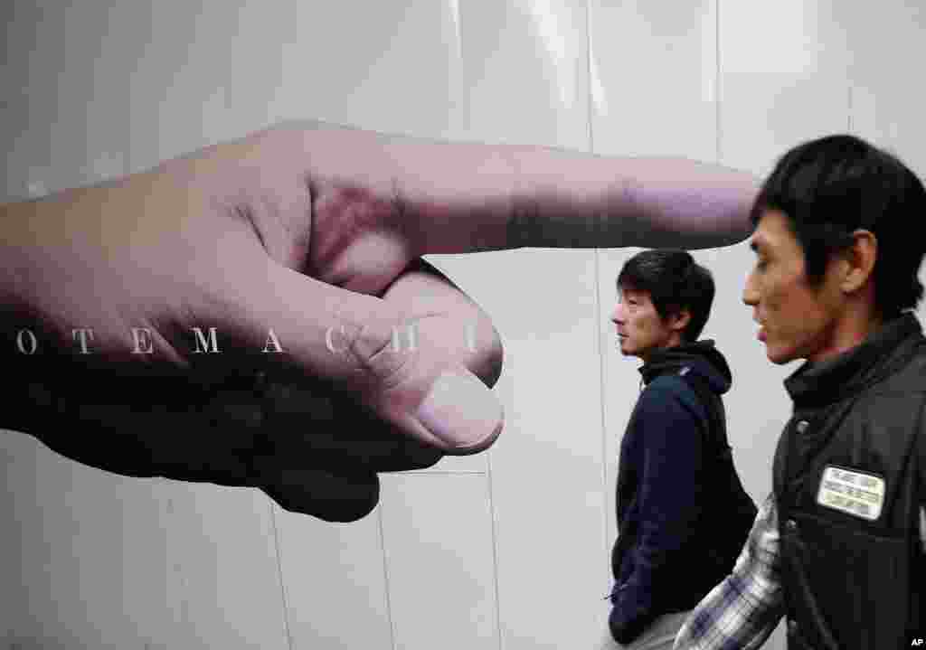 Pria-pria berjalan melewati iklan yang dipasang di pagar lokasi konstruksi di distrik bisnis Otemachi, Tokyo, Jepang. 