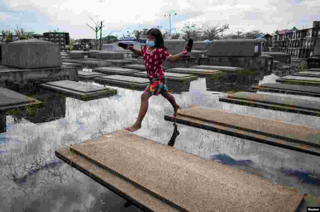 A girl jumps from a tomb, a day before the nationwide cemetery closure during All Saints' Day at a flooded cemetery in Masantol, Pampanga, Philippines.