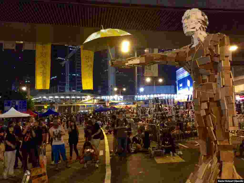 Patung kayu berjudul "Umbrella Man" duduk di tengah tempat demonstrasi di Hong Kong (5/10).