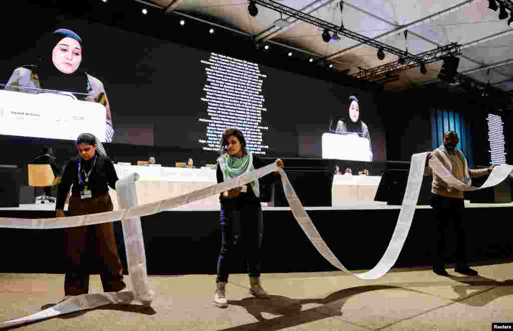 Activists hold a roll of paper with the names of the victims of the conflict between Israel and Hamas as an activist delivers a speech during the "People's Plenary" at the COP29 United Nations climate change conference, in Baku, Azerbaijan.