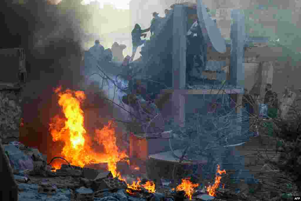 People and rescuers try to put out a fire at the site of an Israeli airstrike that targeted a densely populated neighborhood in Lebanon's eastern city of Baalbek.