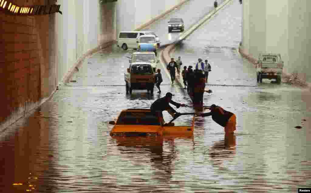 Seorang laki-laki yang mobilnya terperangkap dalam banjir di terowongan dibantu seorang laki-laki lainnya di Sana'a, Yaman.
