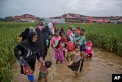 Rohingya Muslims, who crossed over from Myanmar into Bangladesh, wade past a waterlogged path leading to the Jamtoli refugee camp in Ukhiya, Bangladesh, Nov. 17, 2017.