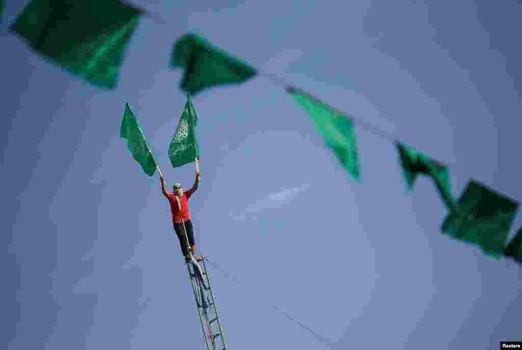 Bunting hangs as a Palestinian holds flags on a ladder at a rally marking the 34th anniversary of Hamas' founding, in the northern Gaza Strip.