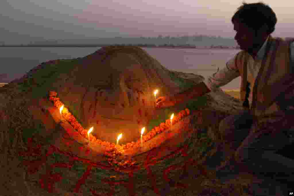 Sand artist Raj Kapoor holds a candle near a sculpture at the Sangam to pay tribute to a gang rape victim who died early Saturday, in Allahabad, Saturday, Dec. 29, 2012.