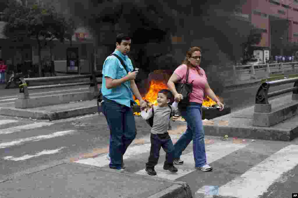People walk in front of a burning barricade blocking the highway in Chacao, Caracas, Feb. 24, 2014.