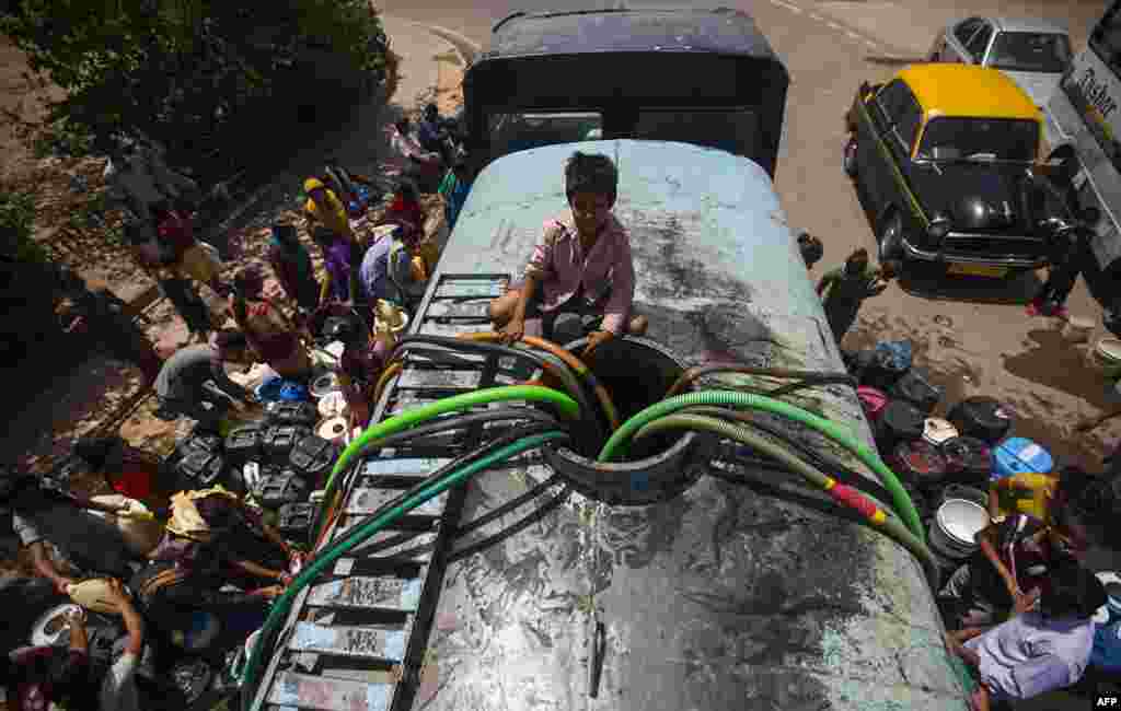 Seorang bocah India duduk di atas truk pasokan air milik pemerintah sementara warga antri mengisi wadah air di New Delhi.