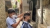 En un callejón del barrio caraqueño La Lucha, Jackner Quevedo atiende a un cliente en una improvisada barbería frente a su casa. Septiembre, 2021. Foto: Adriana Nuñez Rabascall - VOA.
