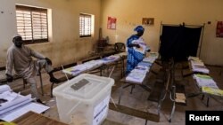 An election worker sits as a woman prepares to cast her vote during parliamentary elections, at a polling station in the Parcelle suburb of Dakar, Senegal, Nov. 17, 2024.