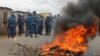 Burundian riot police march past a burning tyre roadblock following clashes with opposition protesters in a street in the capital Bujumbura, April 26, 2015.