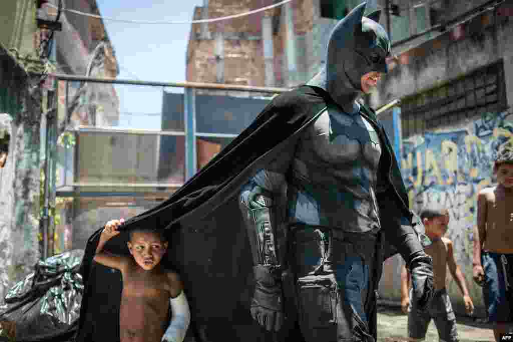 Anak-anak Brazil bermain dengan pria yang memakai pakaian Batman di perkampungan kumuh dekat stadion Maracana, Rio de Janeiro, Brazil.