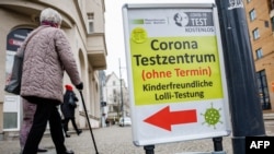 Seorang perempuan lansia berjalan melewati papan petunjuk lokasi tes COVID-19 di pusat kota di Halle / Saale, Jerman timur, 25 Januari 2022, di tengah pandemi. (JENS SCHLUETER / AFP)