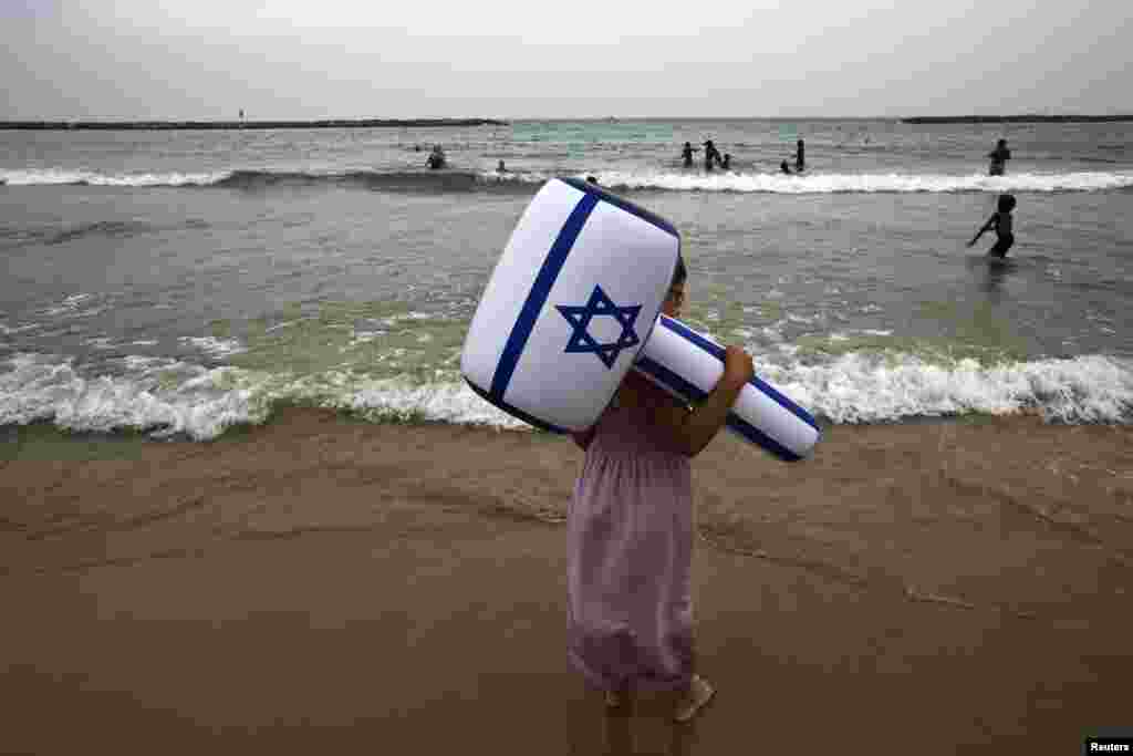 A girl holding to an inflatable hammer in the color of the Israeli flag stands on a beach at Tel Aviv during an aerial show as part of celebrations for Israel's Independence Day to mark the 66th anniversary of the creation of the state.