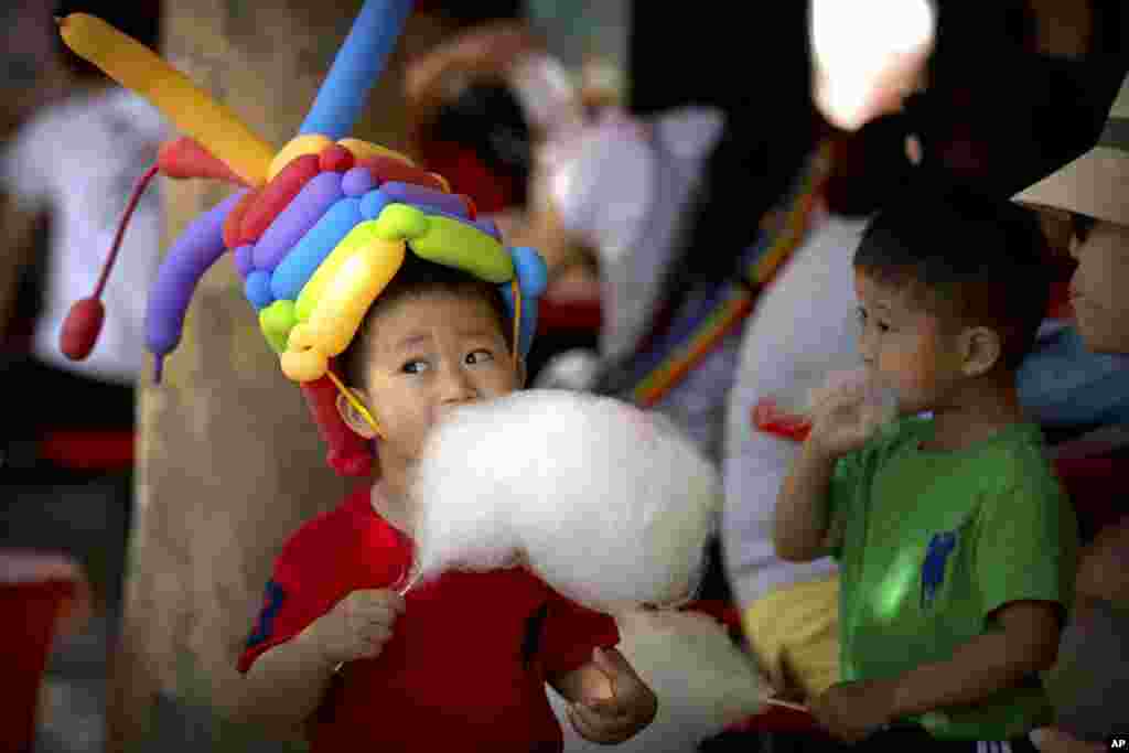 A boy eats cotton candy while wearing a hat made of balloons at a public park in Beijing.