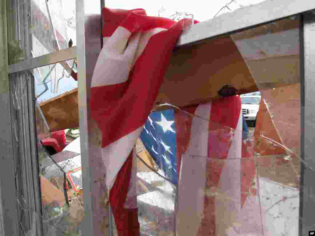 Bendera Amerika terkulai di jendela yang hancur di rumah keluarga Wayne Osmus di Moore, Oklahoma. Keluarga Osmus bersembunyi di lemari Senin (20/5) setelah angin membuat mereka tidak dapat masuk ke tempat perlindungan badai. (AP/Allen Breed)