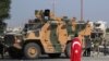 FILE - A boy, with a Turkish flag draped over his shoulders, stands in front of a Turkish military vehicle in the town of Tal Abyad, Syria, Oct. 23, 2019.