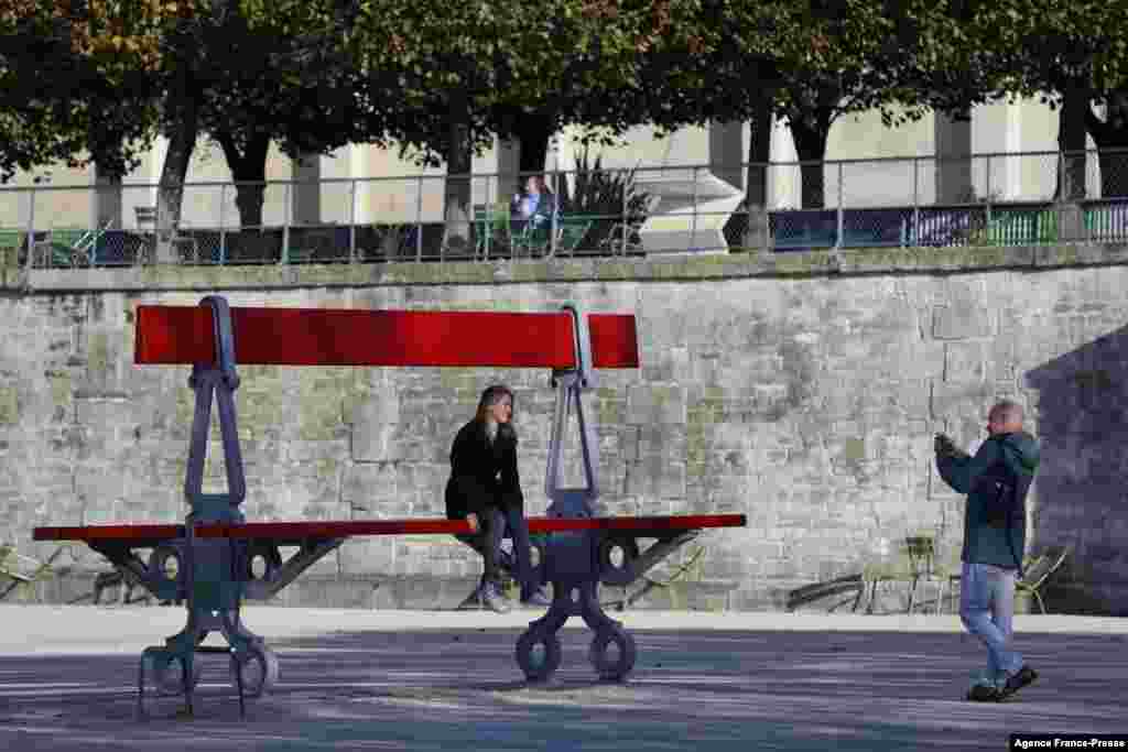 A woman sits on a piece of artwork, "Double Banc," by French artist Lilian Bourgeat, at the French International Contemporary Art Fair, in the Jardin des Tuileries in Paris, France.