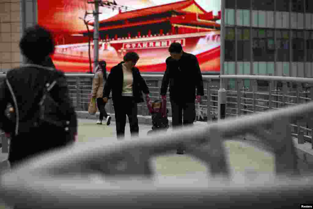 2012年11月8日,一户人家从上海一座天桥上树立的大型宣传屏幕前走过。