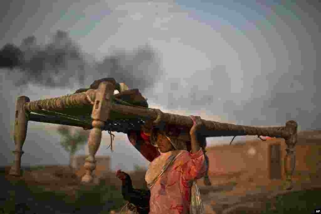 A Pakistani woman carrying a bed on her head and holding a rooster,  walks back to her home through a brick factory on the outskirts of Islamabad, Pakistan.