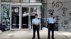香港警察2019年7月2日站在立法会外被抗议者前一晚示威时涂写在外墙上的涂鸦前。