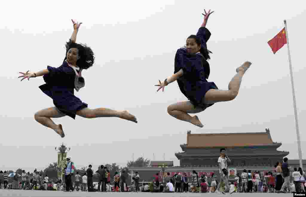 Dua orang yang baru lulus melompat ketika foto mereka diambil di depan GerbangTiananmen dan potret raksasa mending pemimpin China Mao Zedong, di alun-alun Tiananmen di Beijing, China, 19 Juni 2014. 