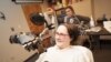 Jan Scheuermann, who has quadriplegia, brings a chocolate bar to her mouth using a robot arm she is guiding with her thoughts. Researcher Elke Brown, M.D., watches in the background, Photo credit: "UPMC"