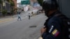 Un miembro de la Policía Nacional Bolivariana observa a dos mujeres cruzar una avenida vacía durante enfrentamientos entre policías y presuntos integrantes de una banda criminal en los alrededores del barrio La Cota 905 de Caracas. Julio 8, 2021.