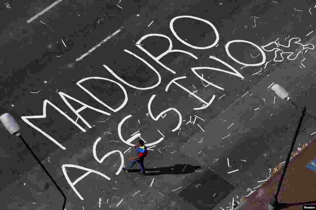 An opposition supporter walks past words painted on a blocked street, reading 'Maduro murderer', at Altamira Square in Caracas, Feb. 21, 2014.