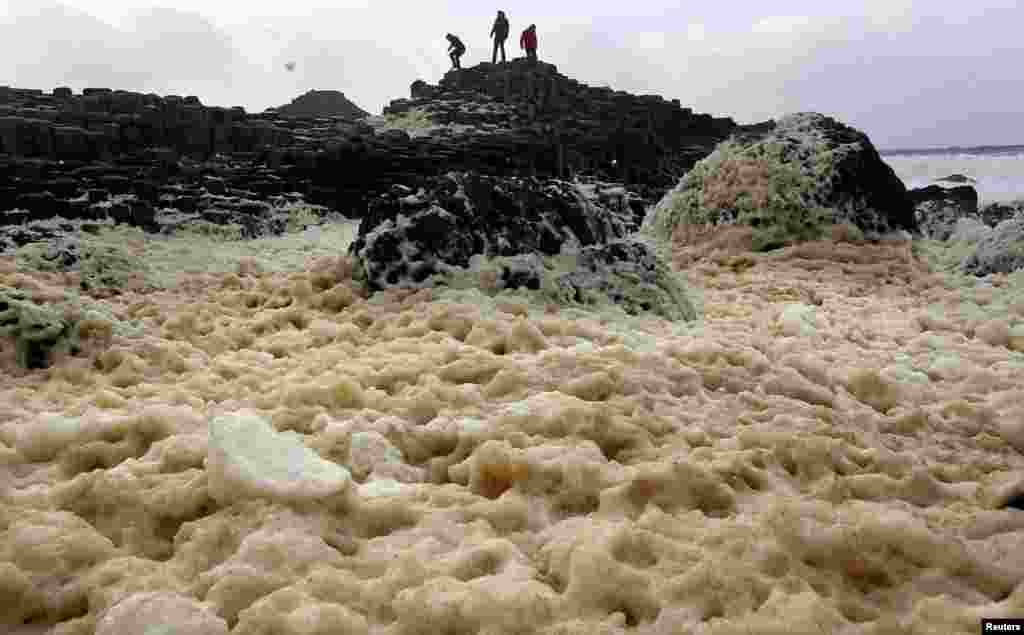Para wisatawan berdiri di pantai utara dekat kota Bushmills di Irlandia utara.