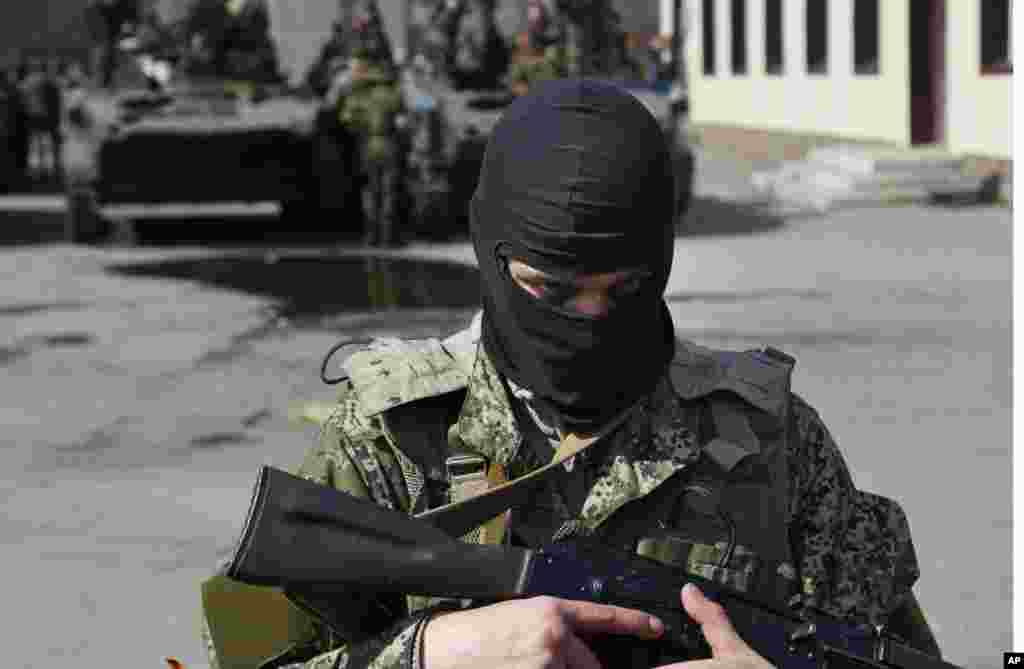 A masked gunman guards combat vehicles with Russian, Donetsk Republic and Ukrainian paratroopers, flags and gunmen on top, Slovyansk, Ukraine, April 16, 2014.