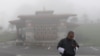 a Bhutanese man looks at his phone on a foggy day at Dochula Pass.