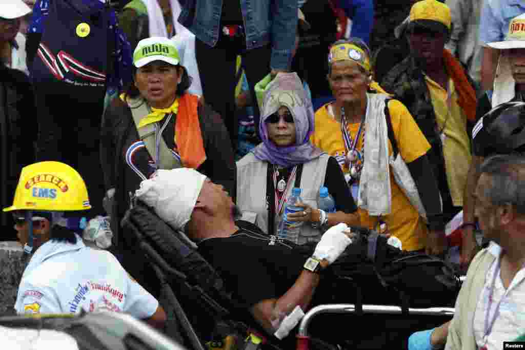 Para demonstran anti-pemerintah melihat seorang pria terluka dibawa dari lokasi bentrokan di kompleks polisi, di utara Bangkok (9/5). (Reuters/Kerek Wongsa)